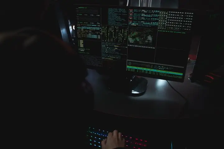 Computer monitors displaying code in a dark cybersecurity workspace.