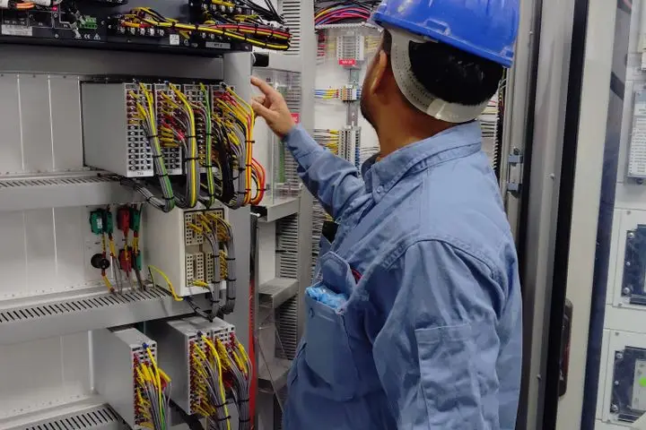 Electrician in safety equipment inspecting an industrial control panel.
