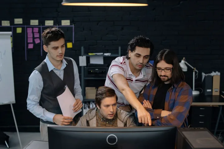 Engineering manager collaborating with a software team around a shared workstation.