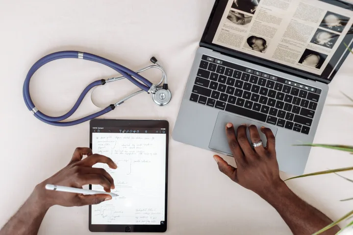 Medical billing and coding professional reviewing digital clinical documentation at a laptop and tablet.