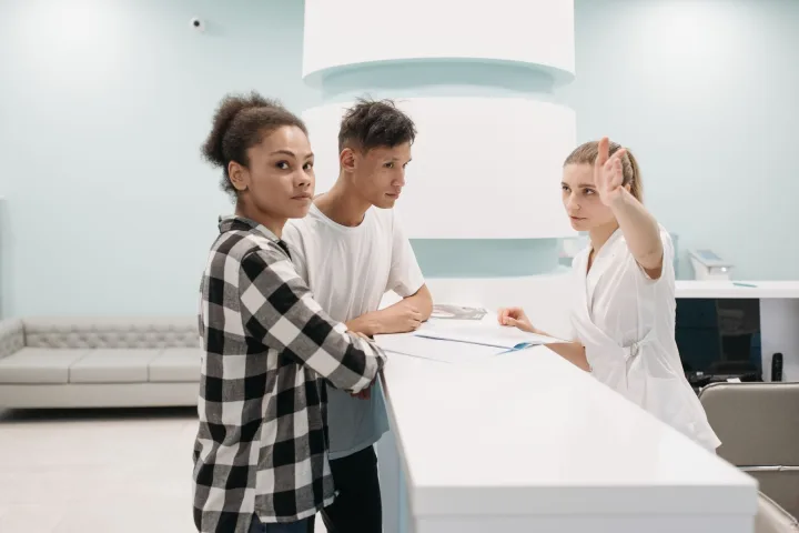 Medical receptionist assisting two patients with registration at a clinic front desk.