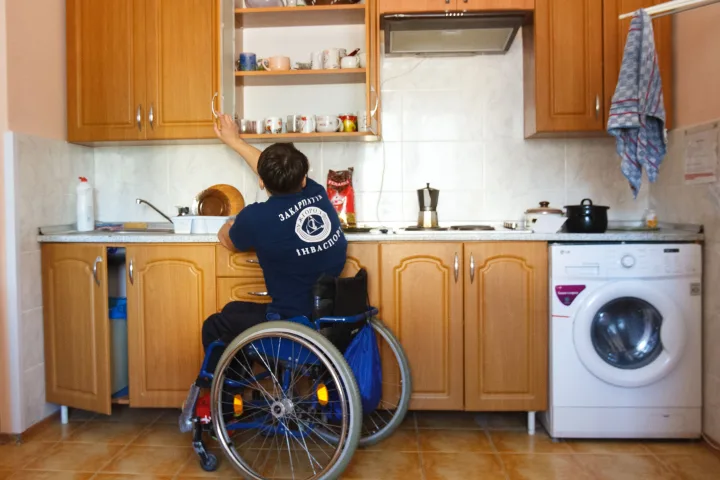 Wheelchair user reaching for kitchen storage while performing an everyday home activity independently.