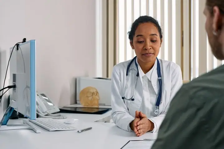 Physician consulting with a patient across a desk in a medical office.