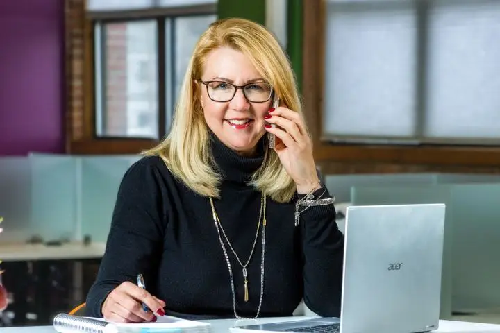Sales development representative speaking with a prospect while taking notes beside a laptop.