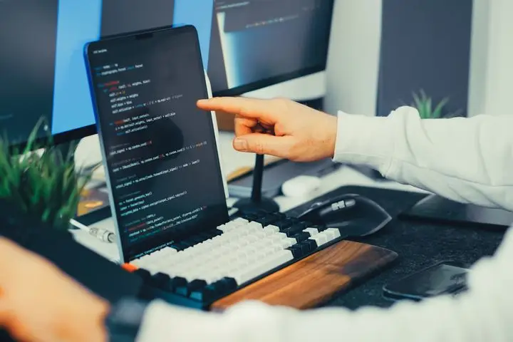 Programmer reviewing code on a laptop and monitor during software testing.