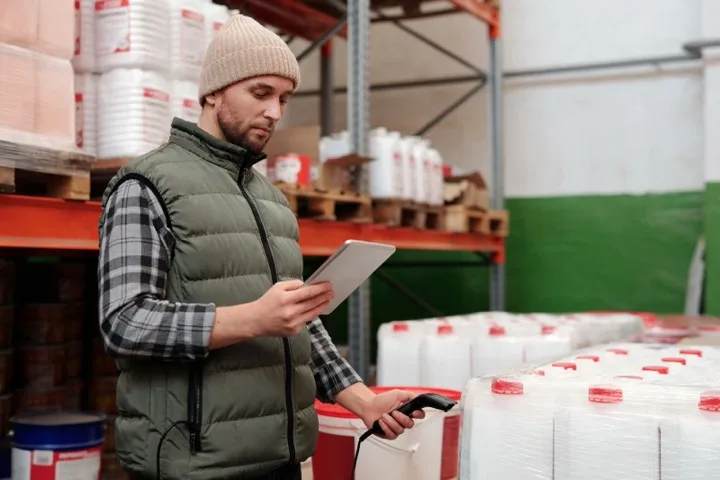 Supply chain analyst reviewing stock information on a tablet beside warehouse inventory.