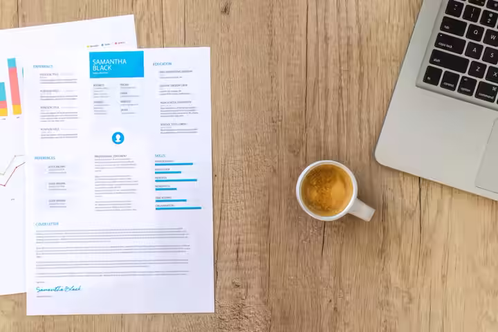 Top view of a desk with resume, coffee cup, and laptop on a wooden surface, ideal for business concepts.