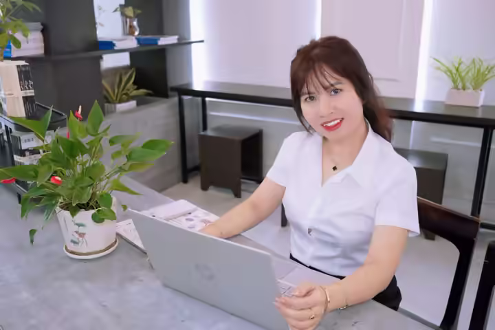 Smiling woman at her desk with laptop in a bright and modern office space.