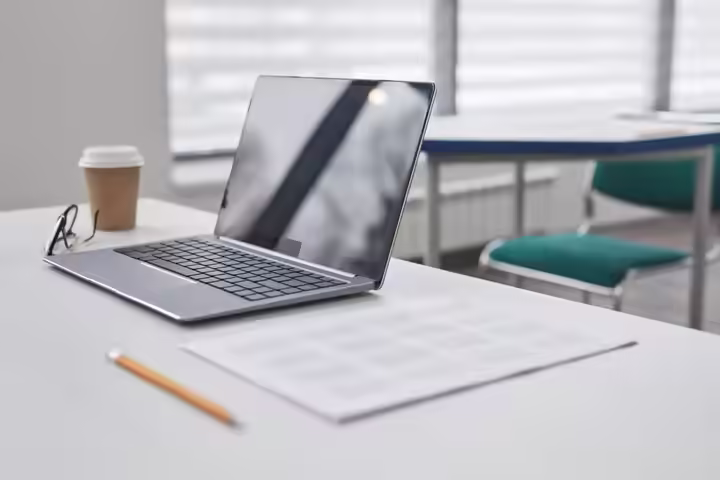 A sleek laptop on a clean white desk, accompanied by a coffee cup, pencil, and glasses in a modern office.