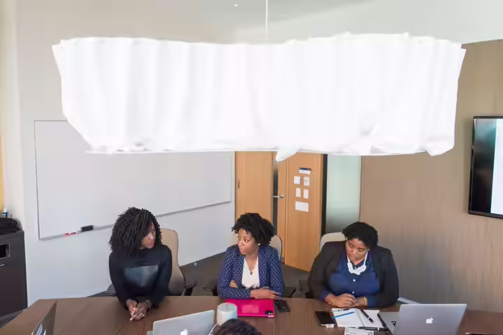 Three women in a modern office engaged in a business meeting with laptops.