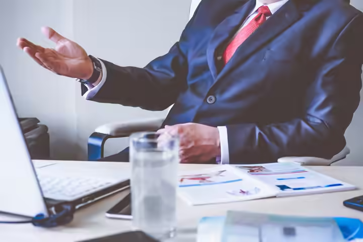 Professional man gesturing in a business meeting at an office desk, conveying confidence and leadership.