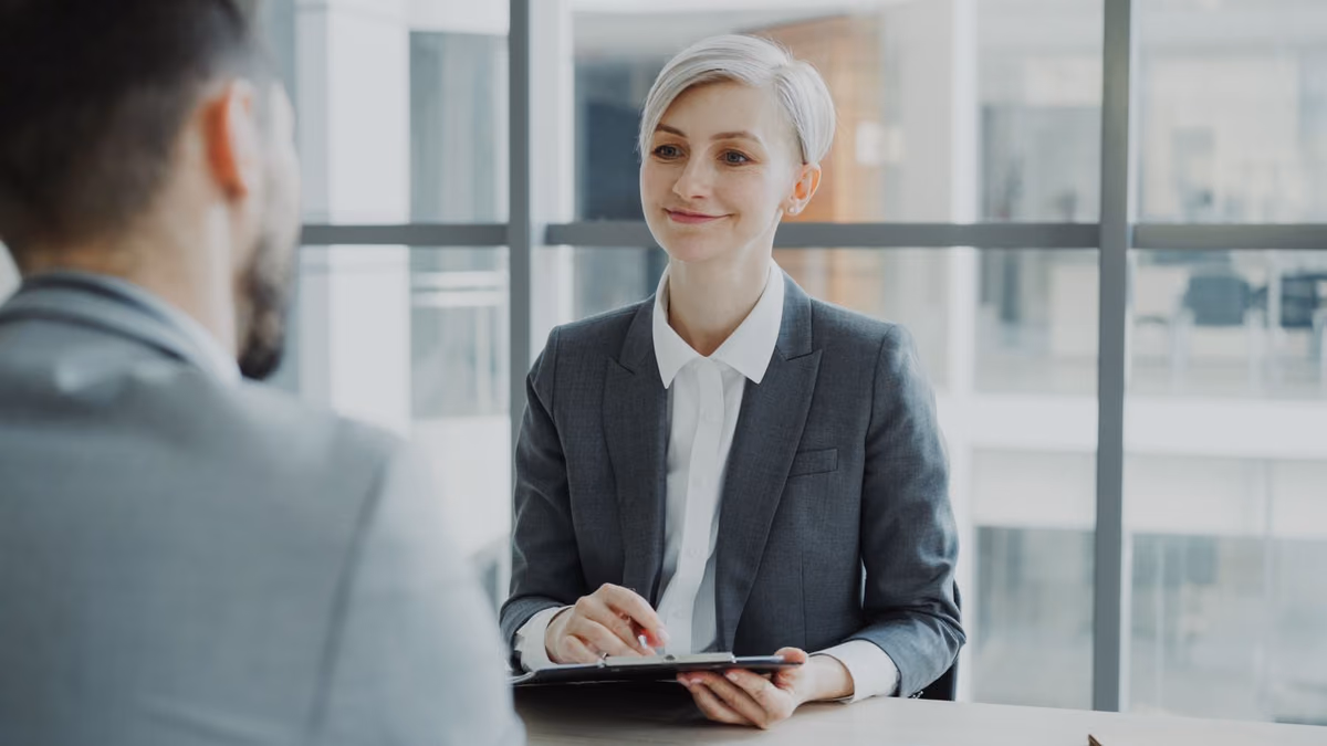 A woman interviews a candidate across a table in a modern office.