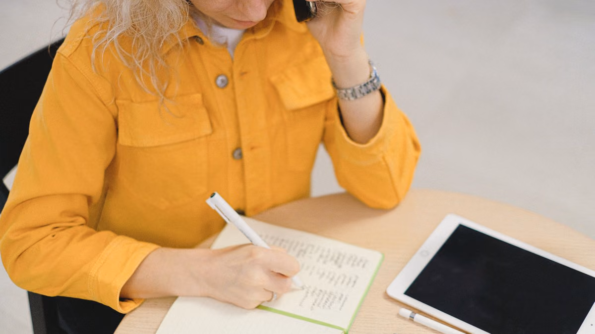 A businesswoman writes notes while speaking on the phone.