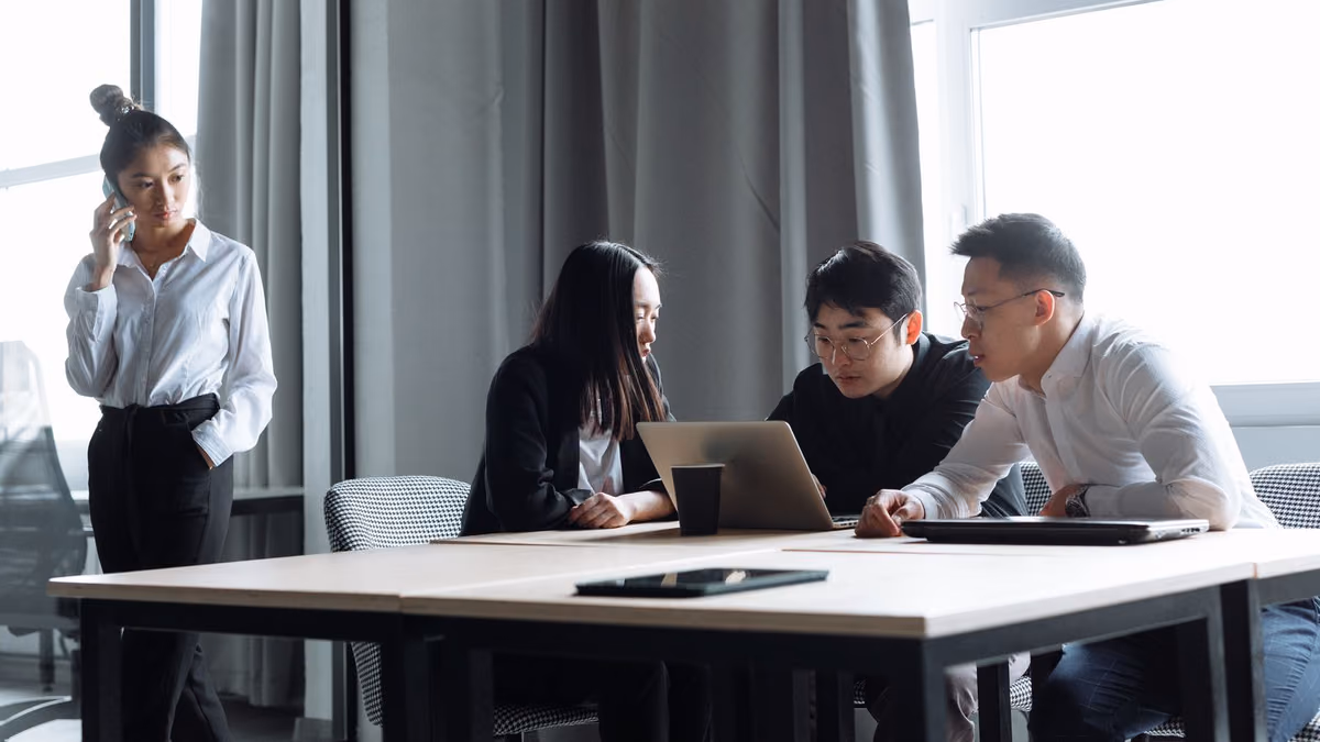 Colleagues discuss a project around a laptop in an office.