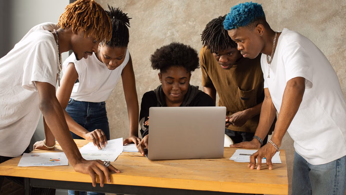 A small group collaborates around a laptop and work materials.