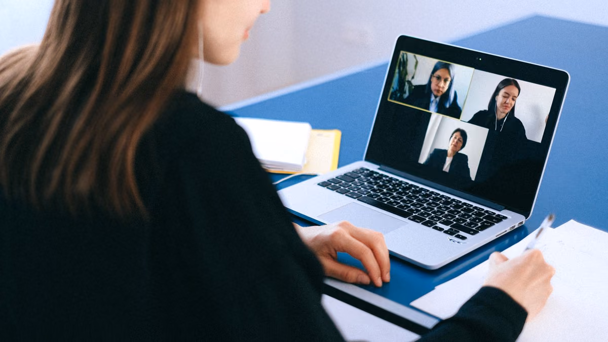 A woman takes notes while speaking on a video call at home.