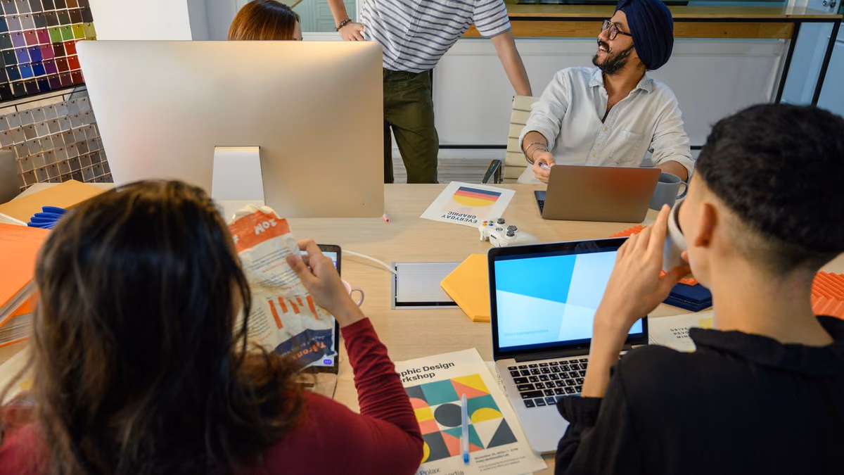 A diverse group collaborates around a laptop in an office.